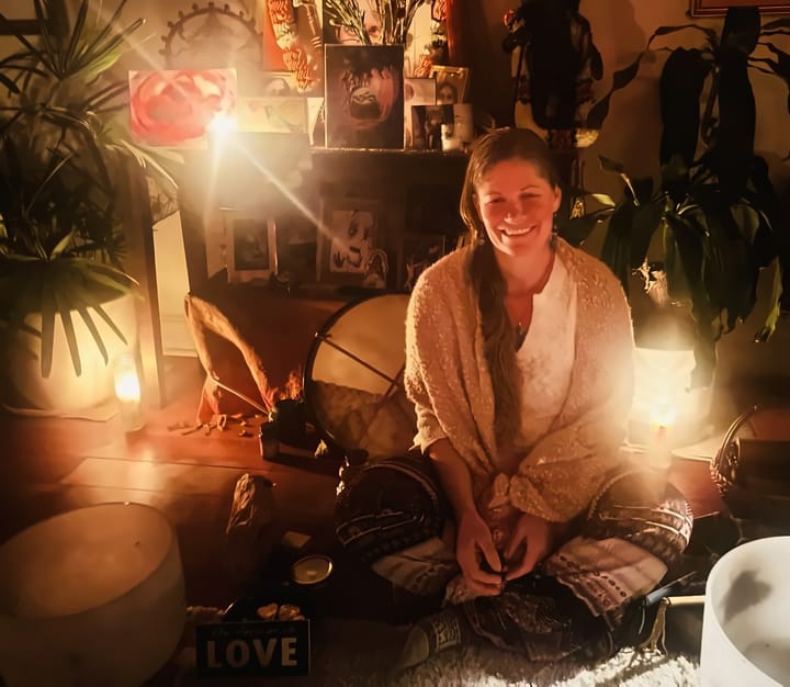 Mayi in a candlelit space with plants and drums
