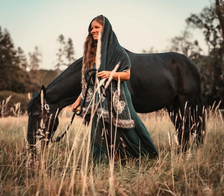 Mayi standing in a golden field with her horse